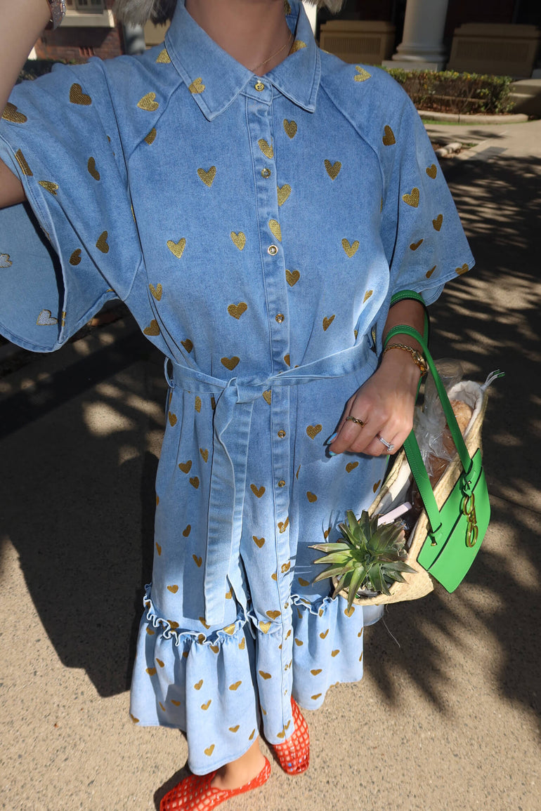 Person wearing a blue dress with gold heart patterns, holding a green bag.