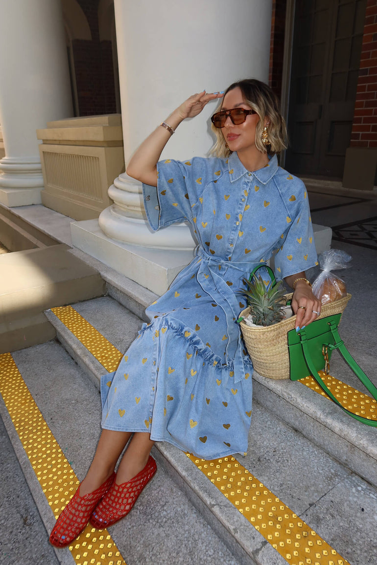 Woman in a blue dress with yellow polka dots sitting on steps, holding a green bag with a pineapple.