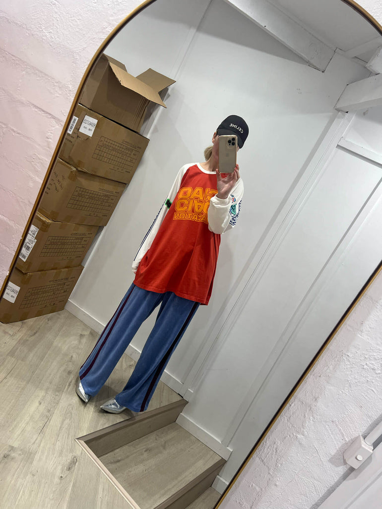 Person wearing a red tank top and blue Terry towelling pants taking a mirror selfie.