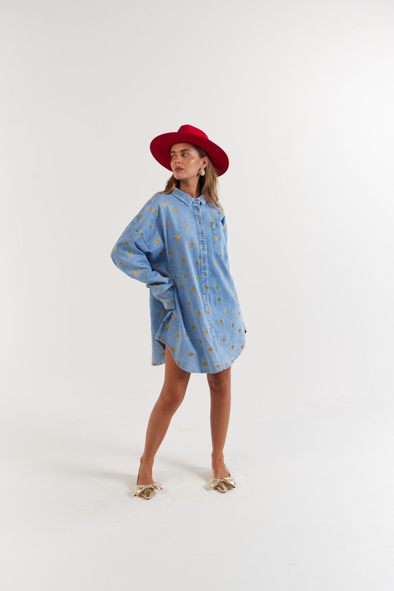 Woman wearing a blue denim dress with gold heart pattern and a red hat