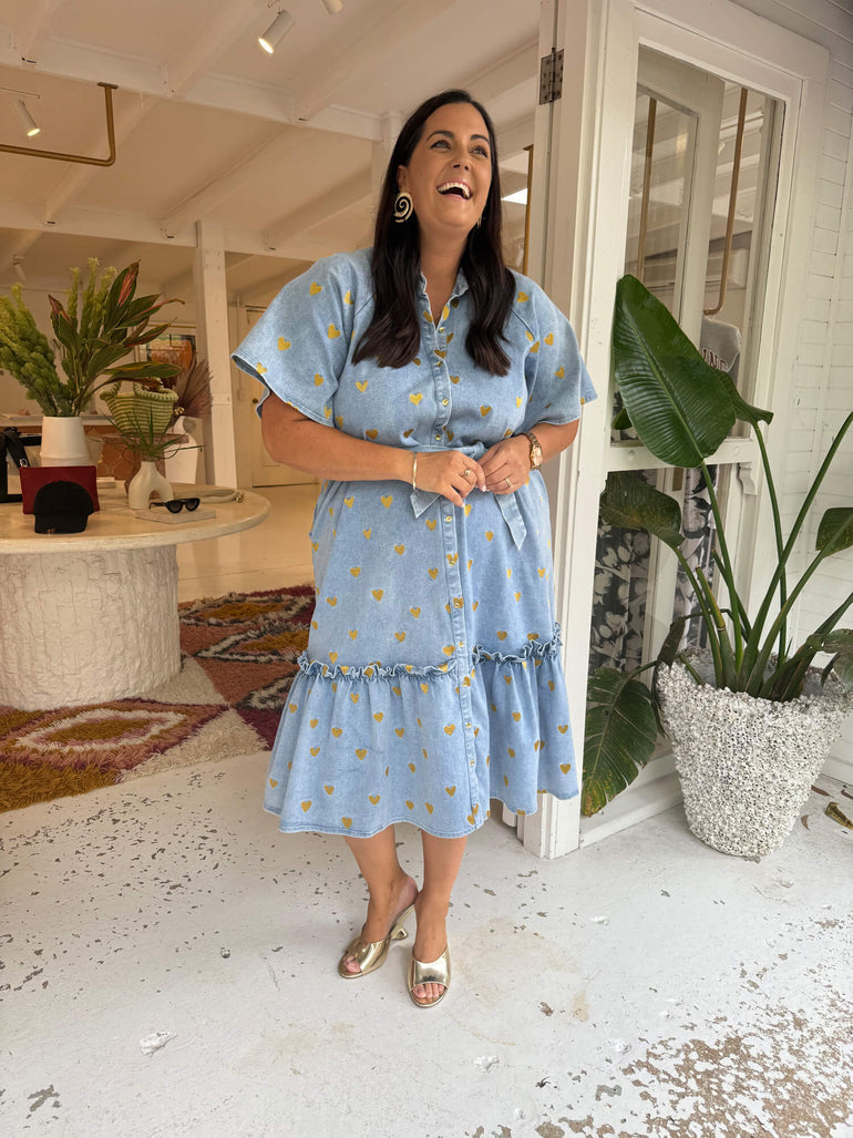 Woman in a blue dress standing in a room with plants and furniture.