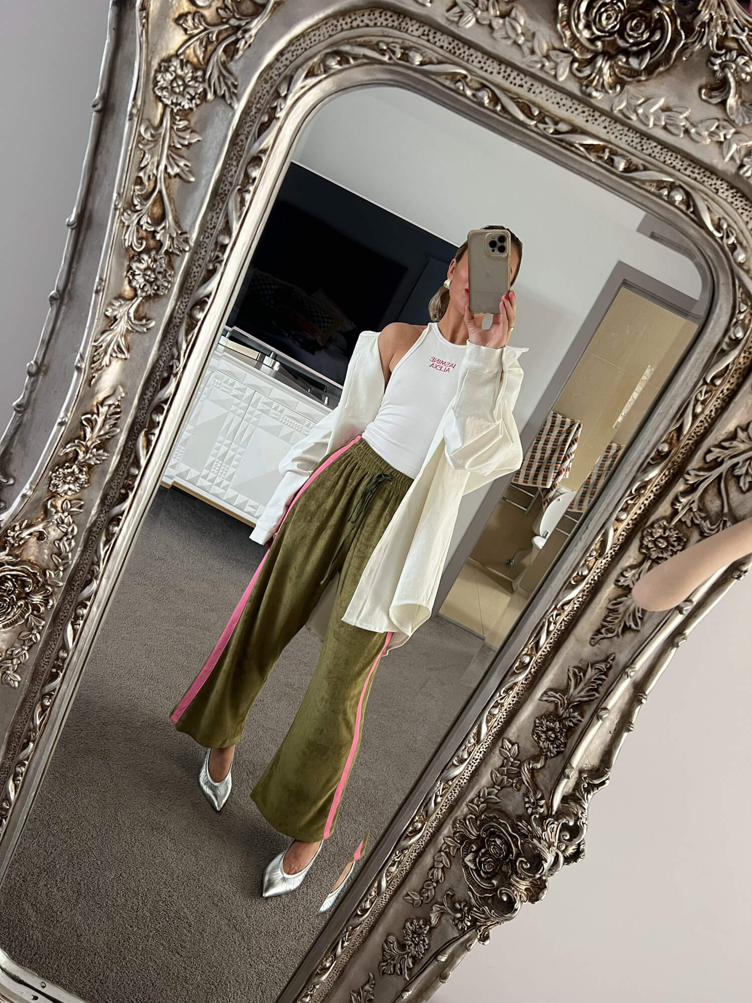 Steph taking a mirror selfie wearing a white shirt and green terry towelling pants with a decorative silver frame.