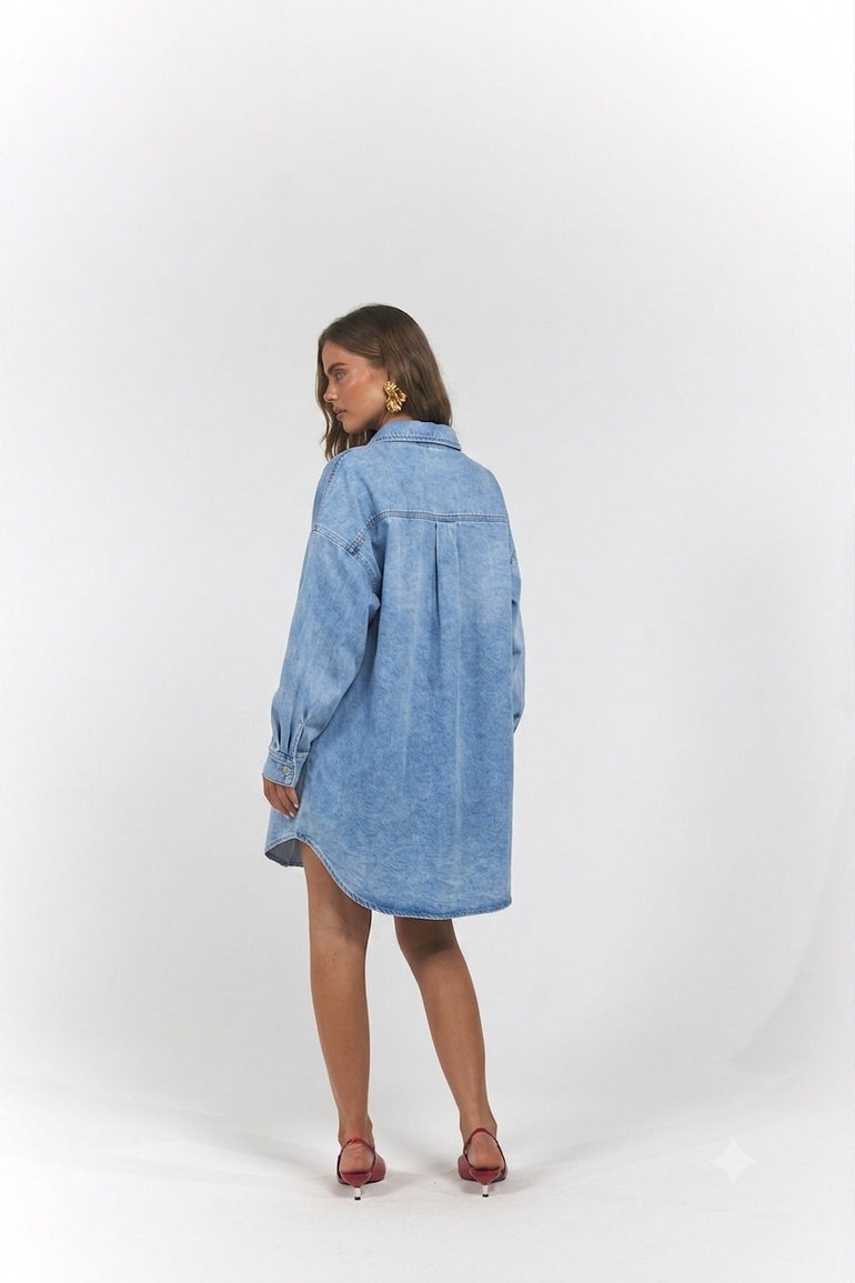 A woman modeling an oversized light blue denim shirt dress, shown from the back.
