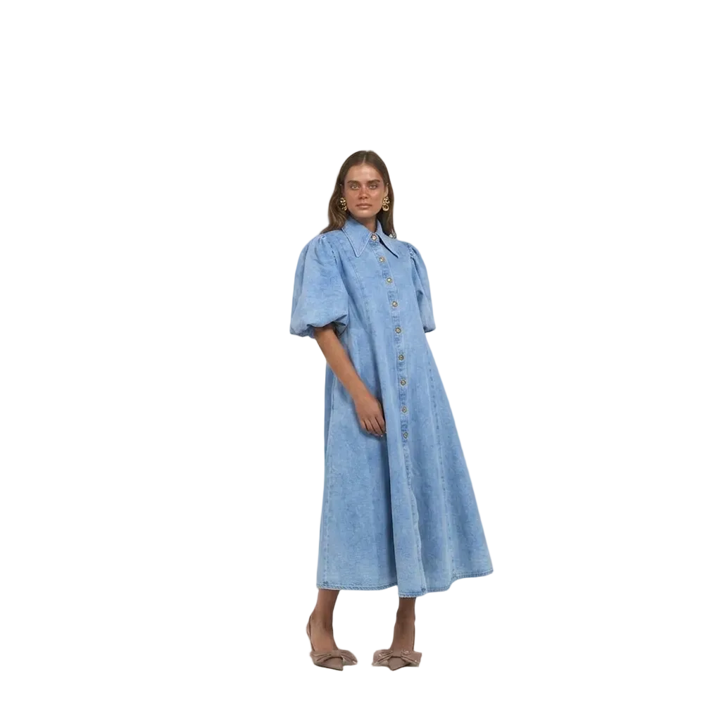 A woman modelling a light blue denim midi dress with puff sleeves, a button-down front, and a high collar.