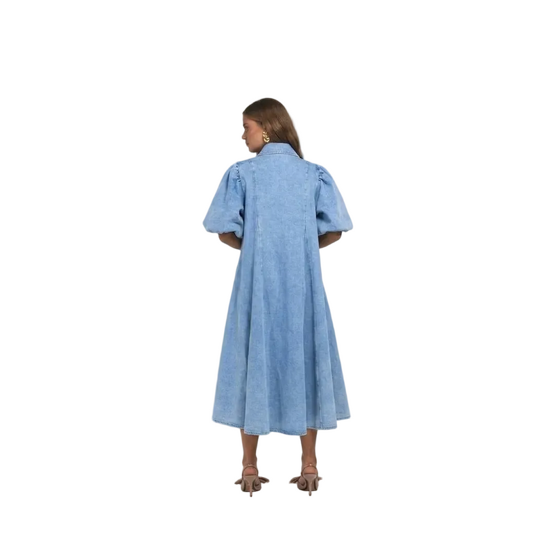 A woman viewed from the back wearing a light blue midi dress with short puff sleeves and a high collar, paired with brown strappy heels.