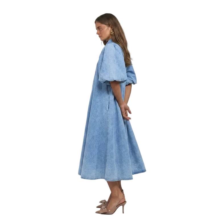 A woman modelling a light blue denim midi dress with voluminous puff sleeves, shown in profile.