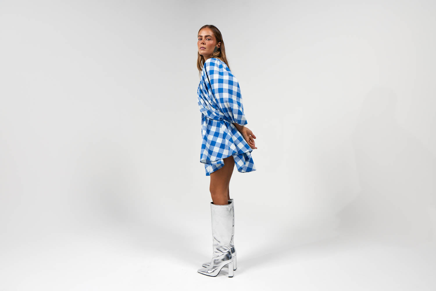 Model wearing blue and gingham printed v neck mini dress with long puff sleeves and silver boots for autumn winter fashion
