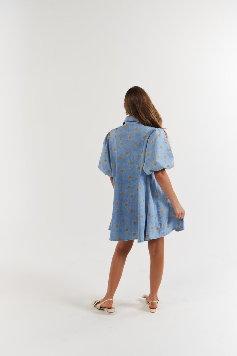 Woman wearing a blue denim dress with gold hearts facing away from the camera