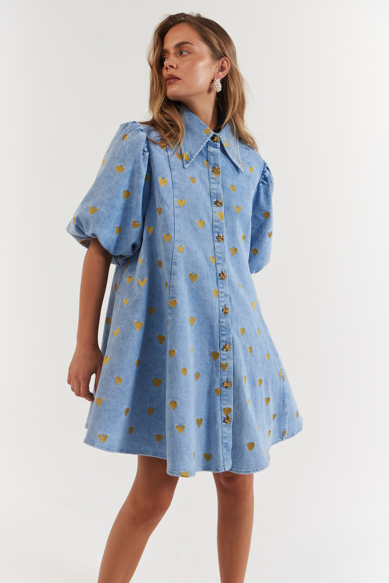 Woman wearing a blue Denim Hearts dress with gold heart patterns