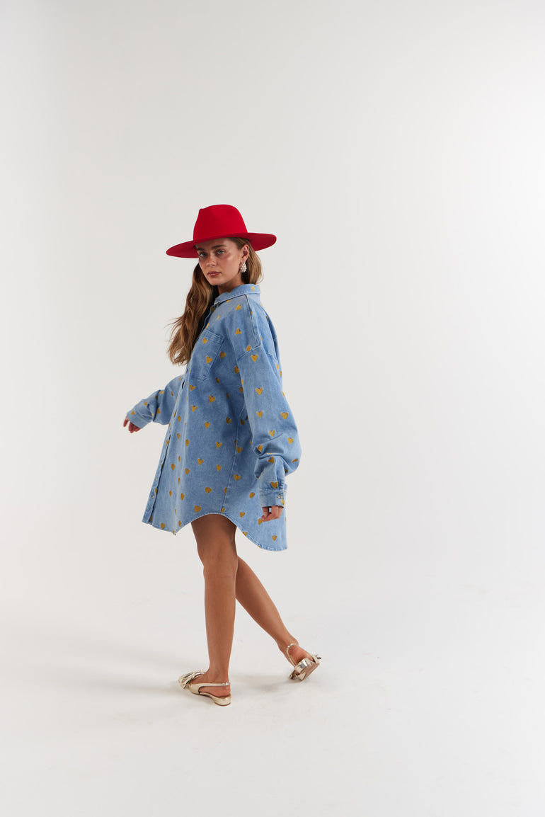 Woman wearing a blue denim dress with gold hearts and a red hat
