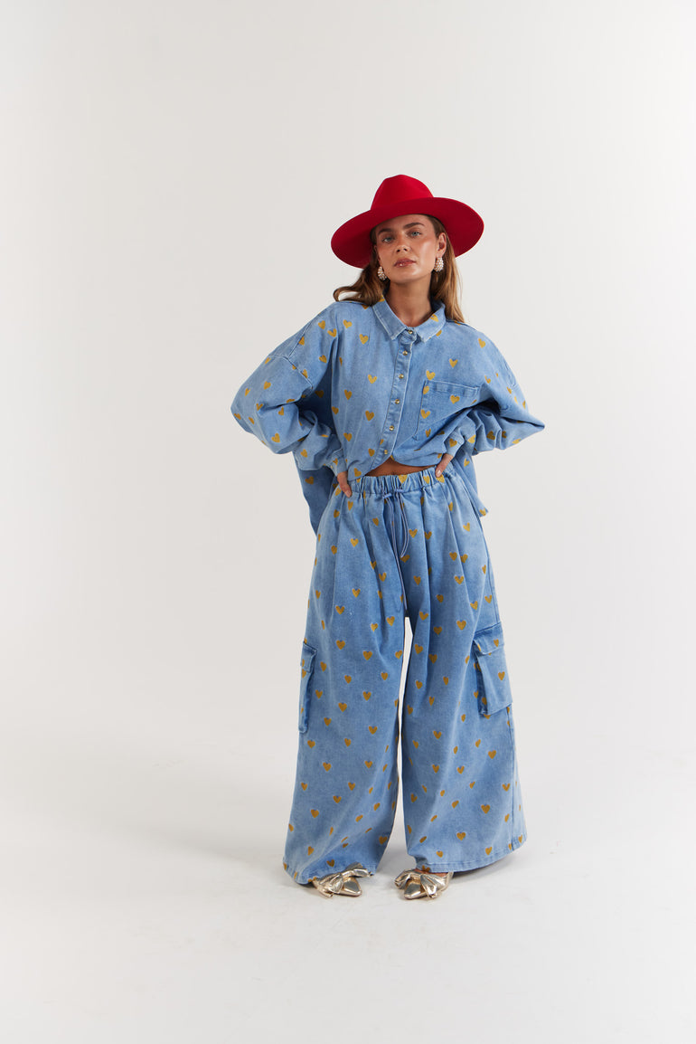 Person wearing a blue denim and gold hearts outfit with a red hat