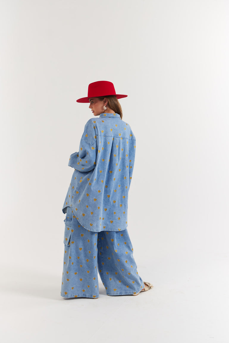 Person wearing a blue denim, gold heart patterned outfit and red hat