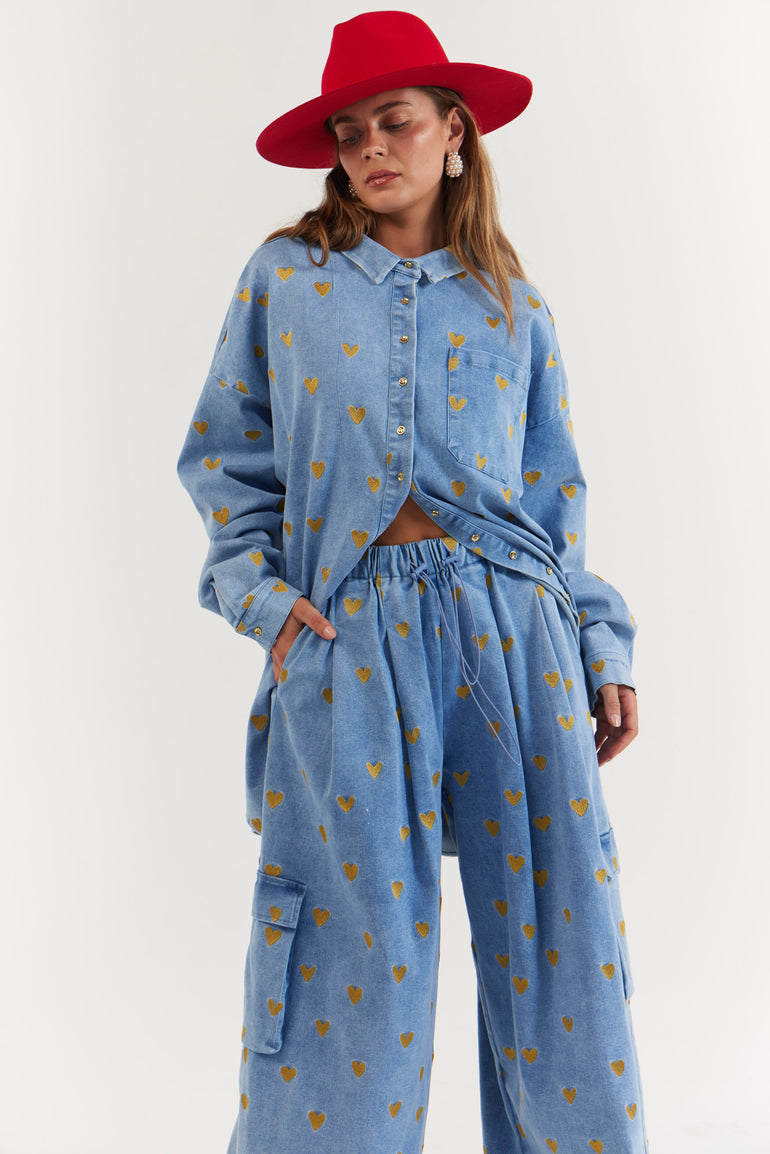 Woman wearing a blue denim outfit with gold heart pattern and a red hat