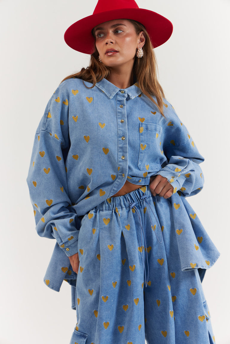 Woman wearing a blue denim outfit with gold heart patterns and a red hat