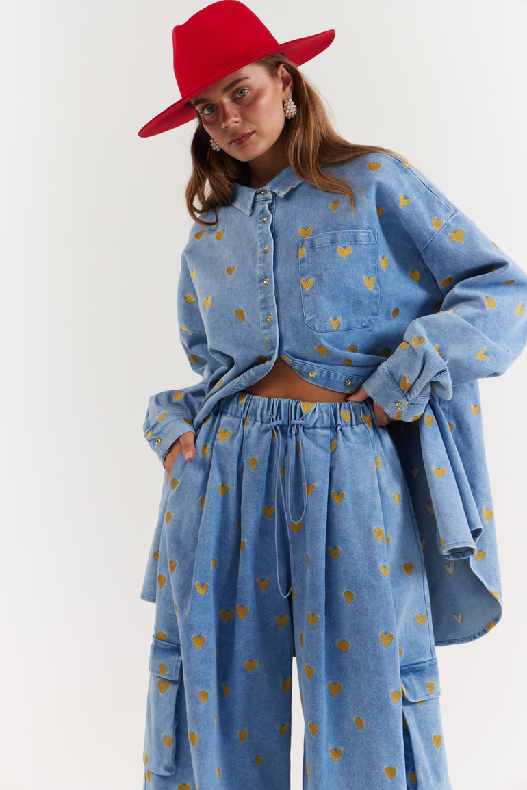 Person wearing a blue denim, gold hearts outfit with yellow heart patterns and a red hat 