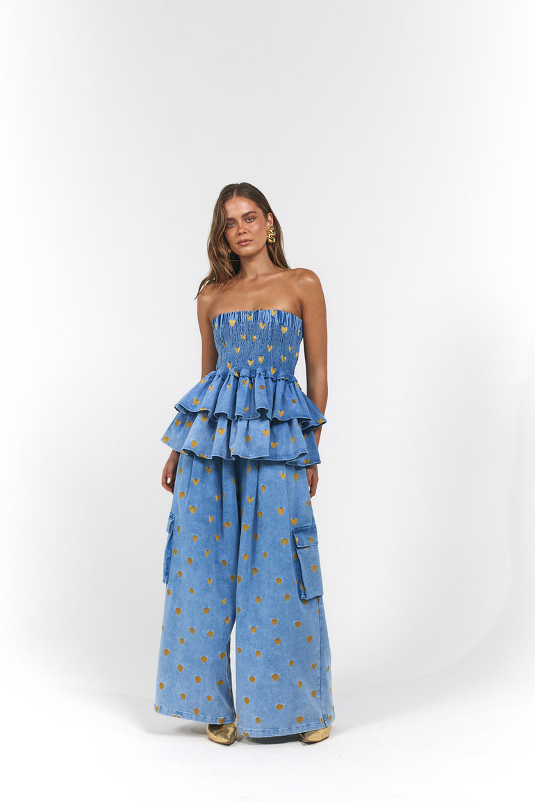 Woman wearing a blue denim, gold hearts strapless top and wide-leg pants with ruffled layers