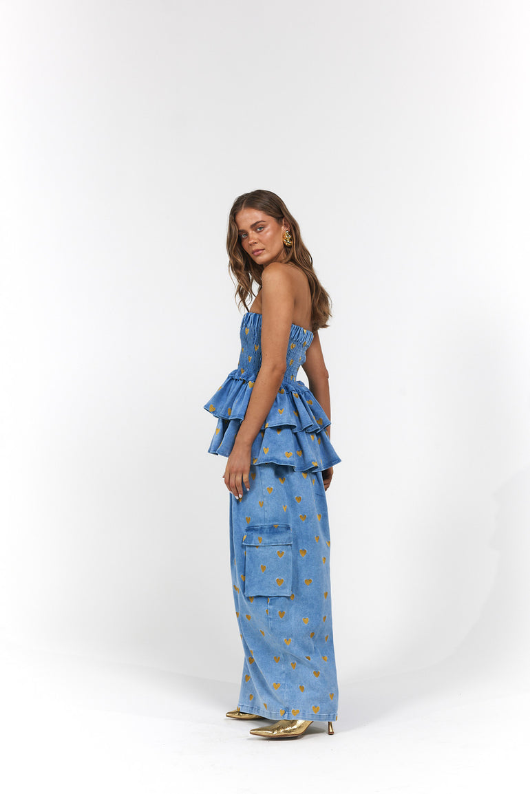 Woman wearing a blue denim, gold hearts strapless top and wide-leg pants with ruffled layers