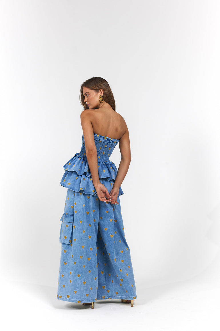 Woman wearing a blue denim, gold hearts strapless top and wide-leg pants with ruffled layers