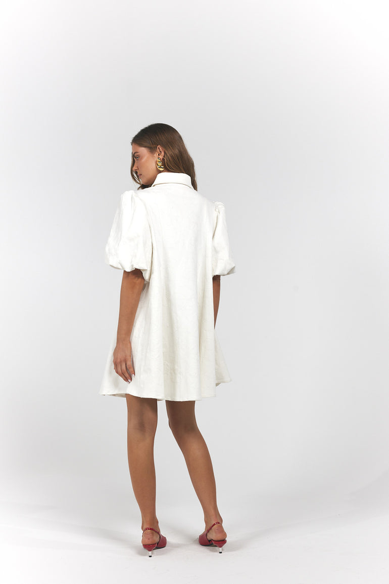 A woman is shown from the back wearing a white puff-sleeve collared dress, paired with dark brown strappy heels.