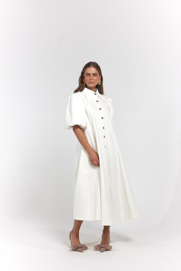 A woman modelling a white midi dress with puff sleeves, a high collar, and gold buttons down the front.