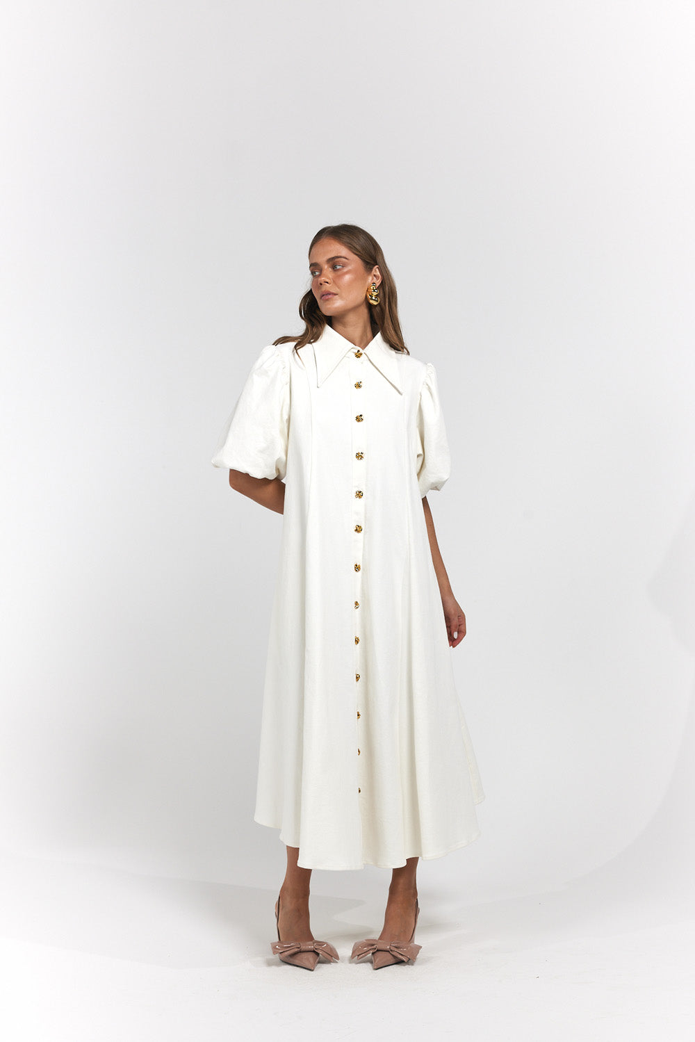 A woman modeling a white midi dress with puff sleeves, a pointed collar, and a front button closure.