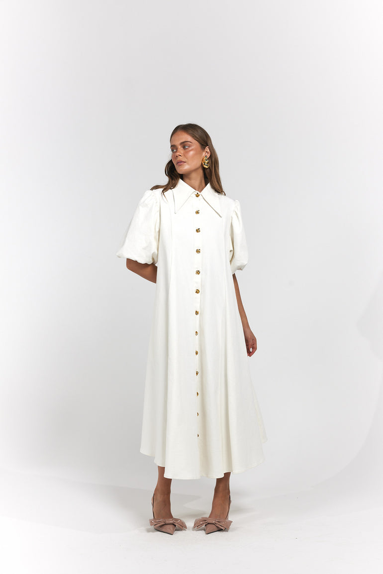 A woman modeling a white midi dress with puff sleeves, a pointed collar, and a front button closure.