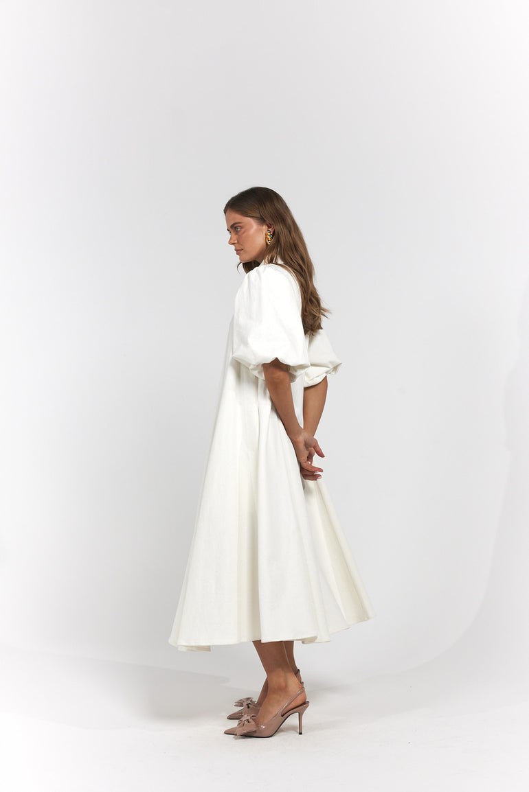 A woman modelling a white midi dress with puffed short sleeves and a flared skirt, shown in profile.