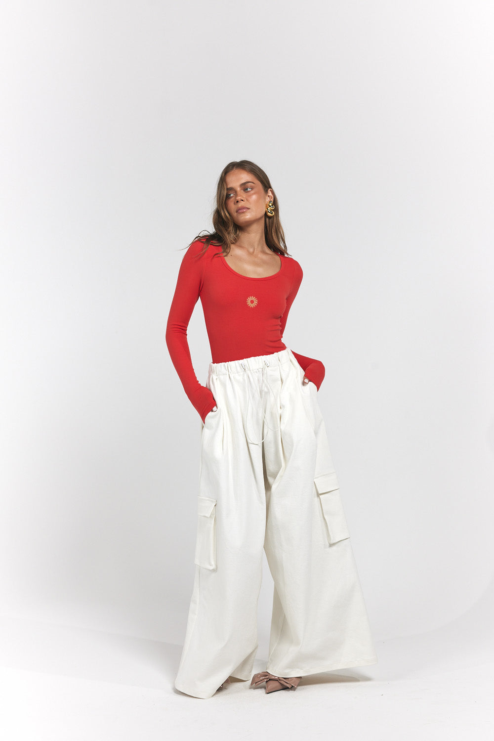 A woman modelling a red long-sleeve scoop-neck top paired with high-waisted, wide-leg white cargo pants.