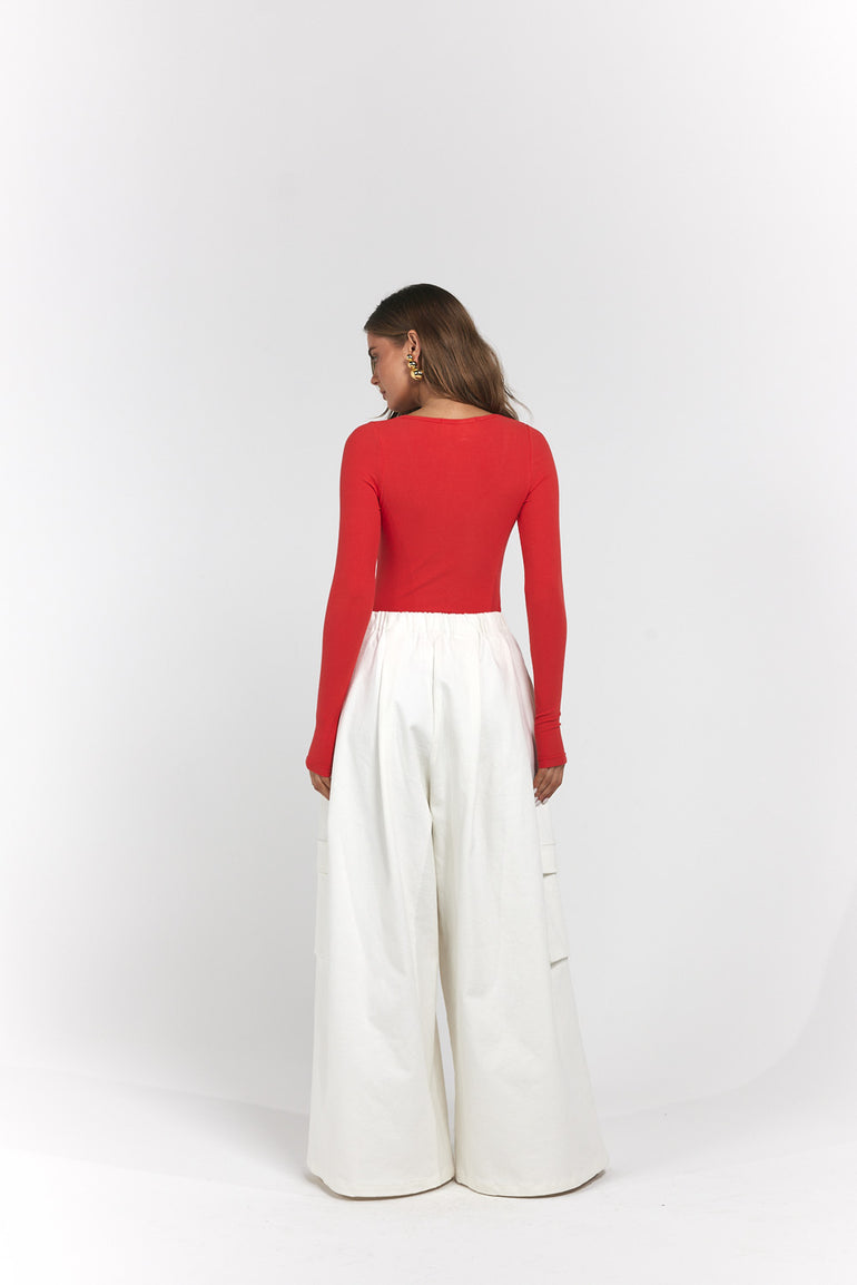 A woman shown from the back wearing a bright red long-sleeve top and high-waisted white wide-leg trousers.