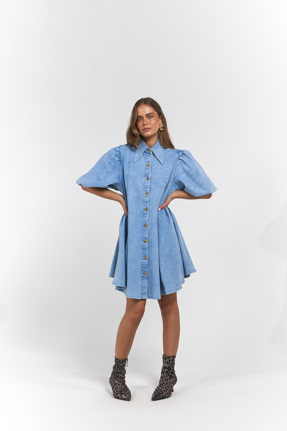 A woman modelling a light blue denim shirt dress with puff sleeves and a button-down front, paired with dark patterned ankle boots.