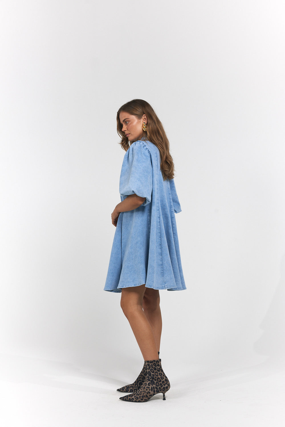 A woman modelling a light blue denim dress with voluminous elbow-length sleeves and a flared skirt, paired with leopard-print ankle boots.