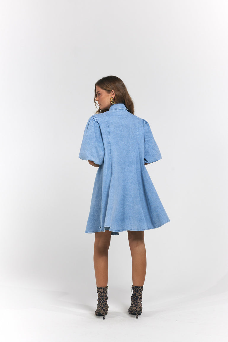 A model is shown from the back wearing a light blue denim short-sleeve dress with a high collar and flared skirt, paired with leopard-print ankle boots.