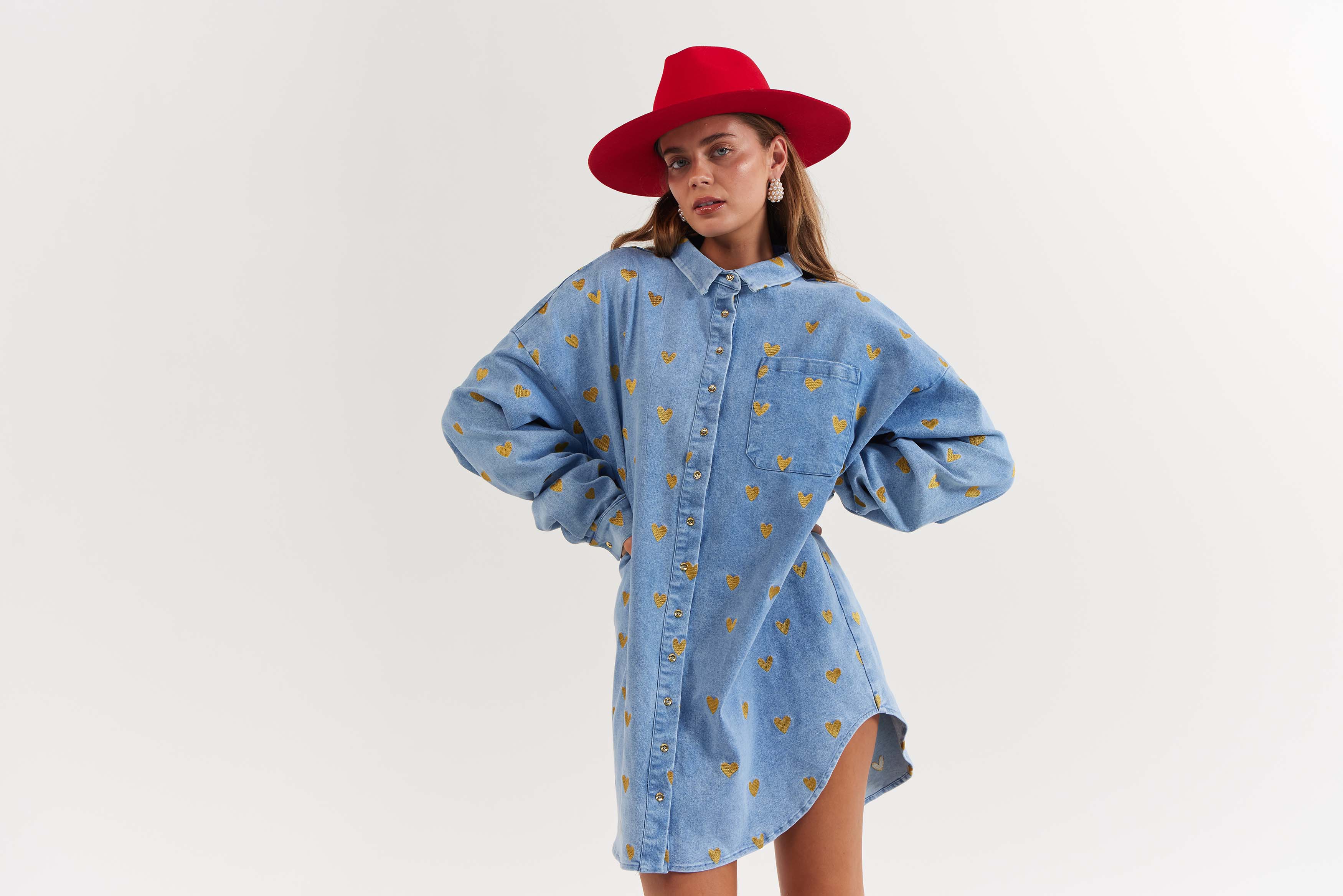 Woman wearing a blue denim dress with heart patterns and a red hat on a white background