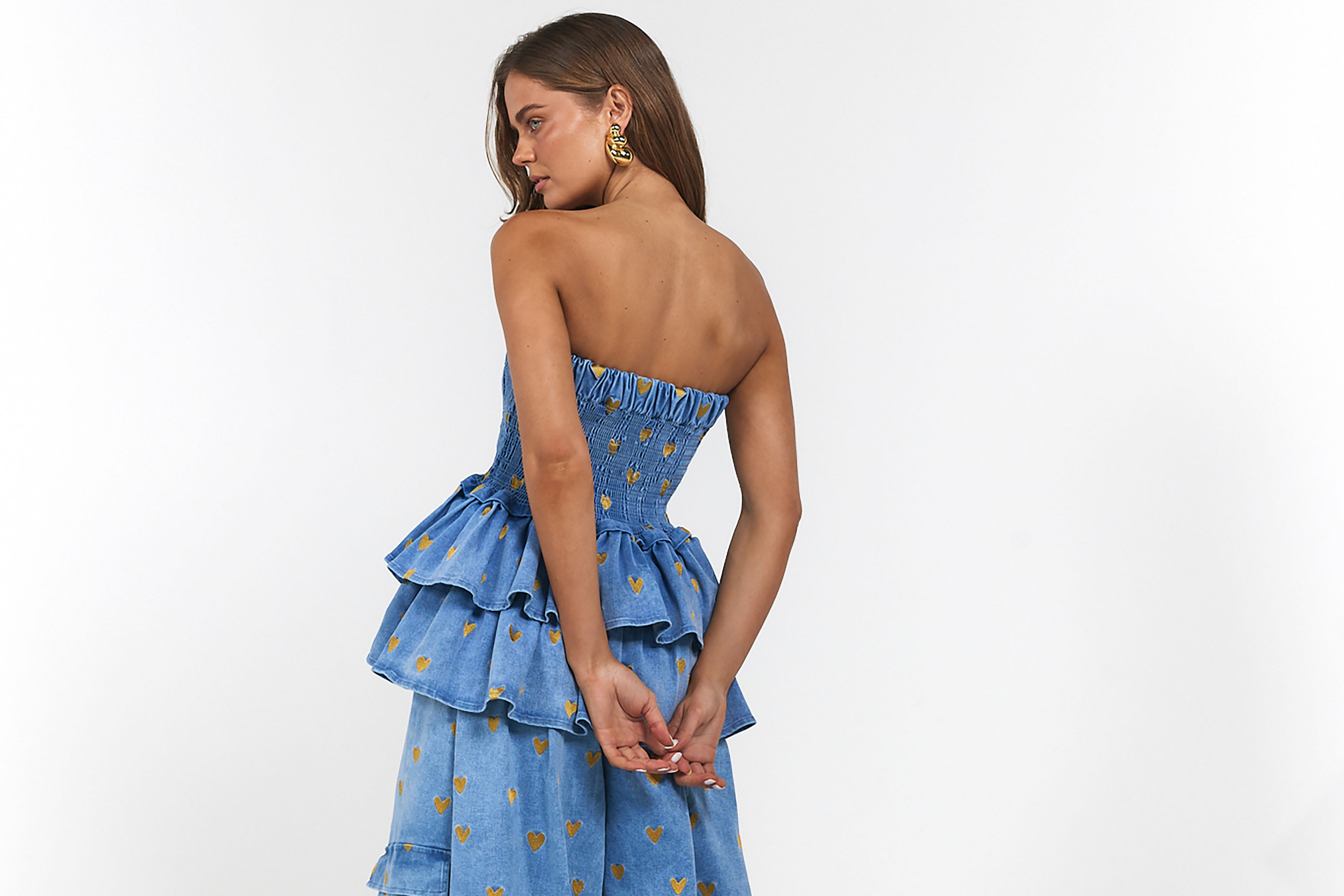 Woman wearing a blue strapless dress with hearts and ruffled layers on a white background