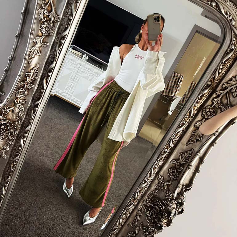 Stephanie Davies taking a mirror selfie wearing a white top and green Viva Terry Pants with a pink stripe. Viva Terry - La Boheme